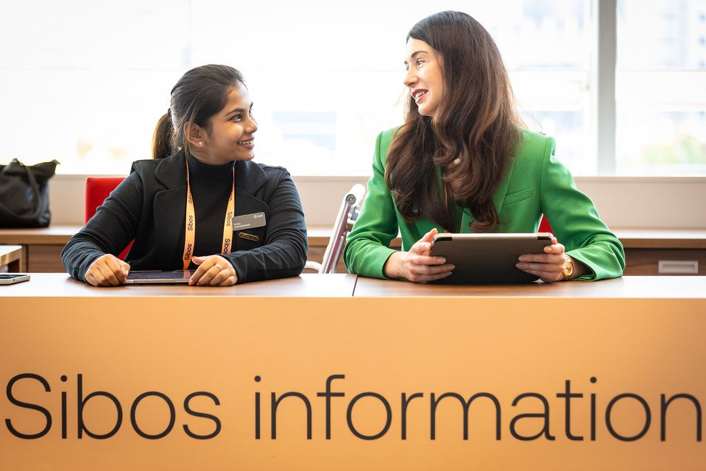 Two staff members helping delegates at a Sibos information desk in 2025