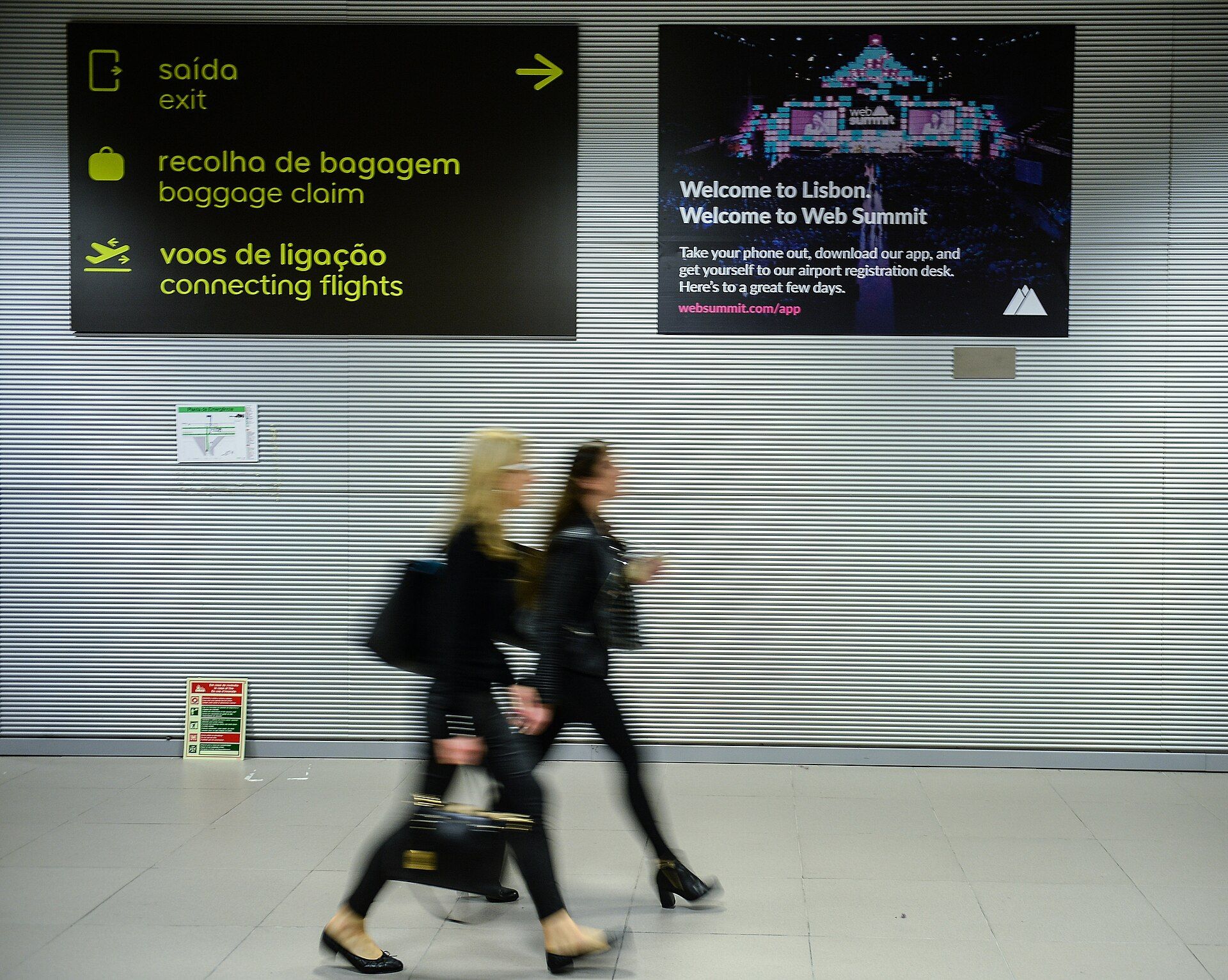 Travelers passing Web Summit welcome signage at Lisbon Airport